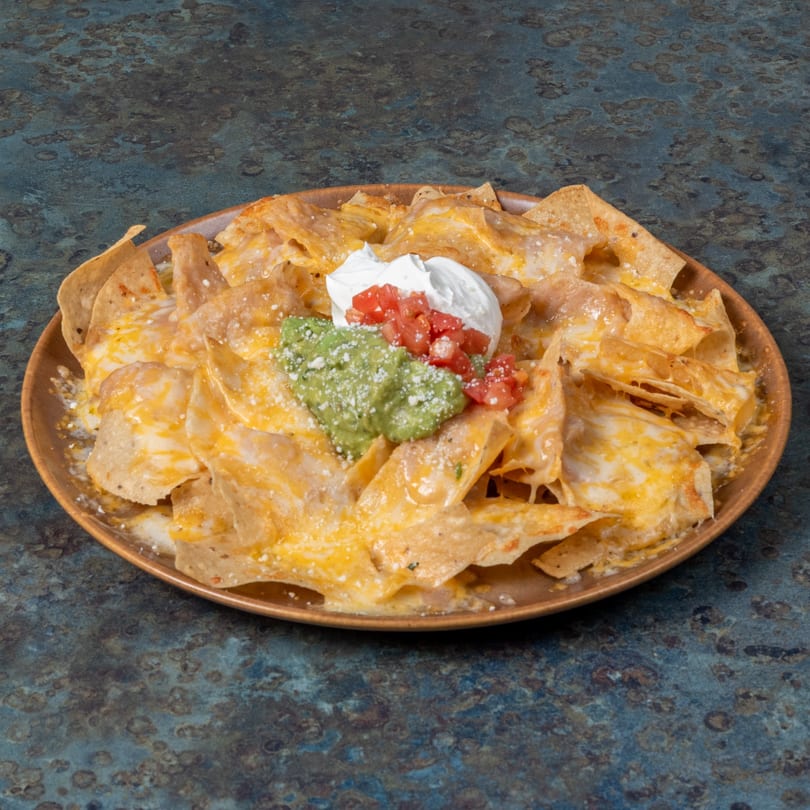 El Ranchero's cheesy nachos with guacamole, sour cream, and diced tomatoes on a rustic plate.