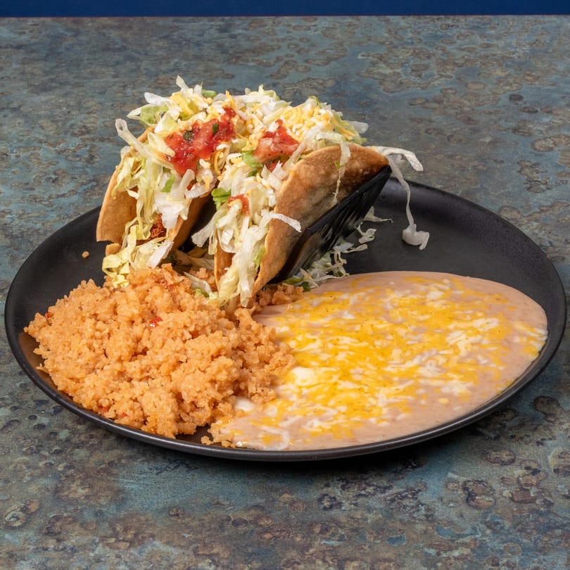 Two crispy El Ranchero tacos with lettuce, cheese, and tomatoes, served with rice and refried beans.