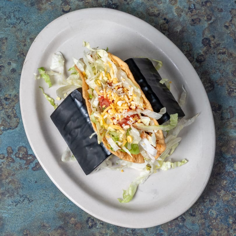 A crispy El Ranchero taco filled with seasoned meat, shredded lettuce, diced tomatoes, and cheese.