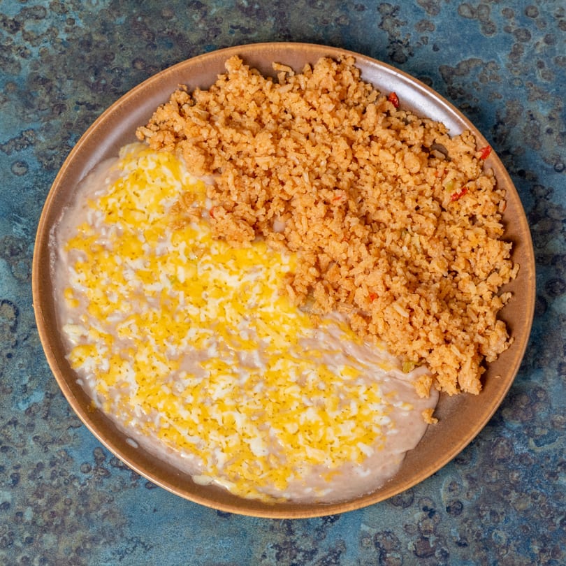 A plate of El Ranchero's Mexican rice and refried beans topped with melted cheese.