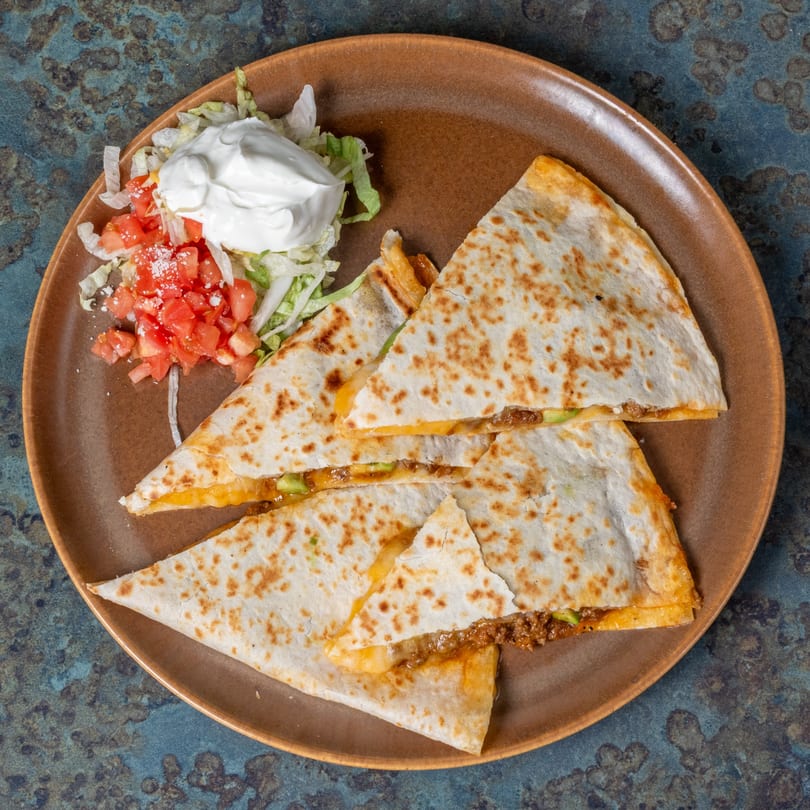 El Ranchero's beef quesadilla with melted cheese, served with a side of lettuce, diced tomatoes, and sour cream.