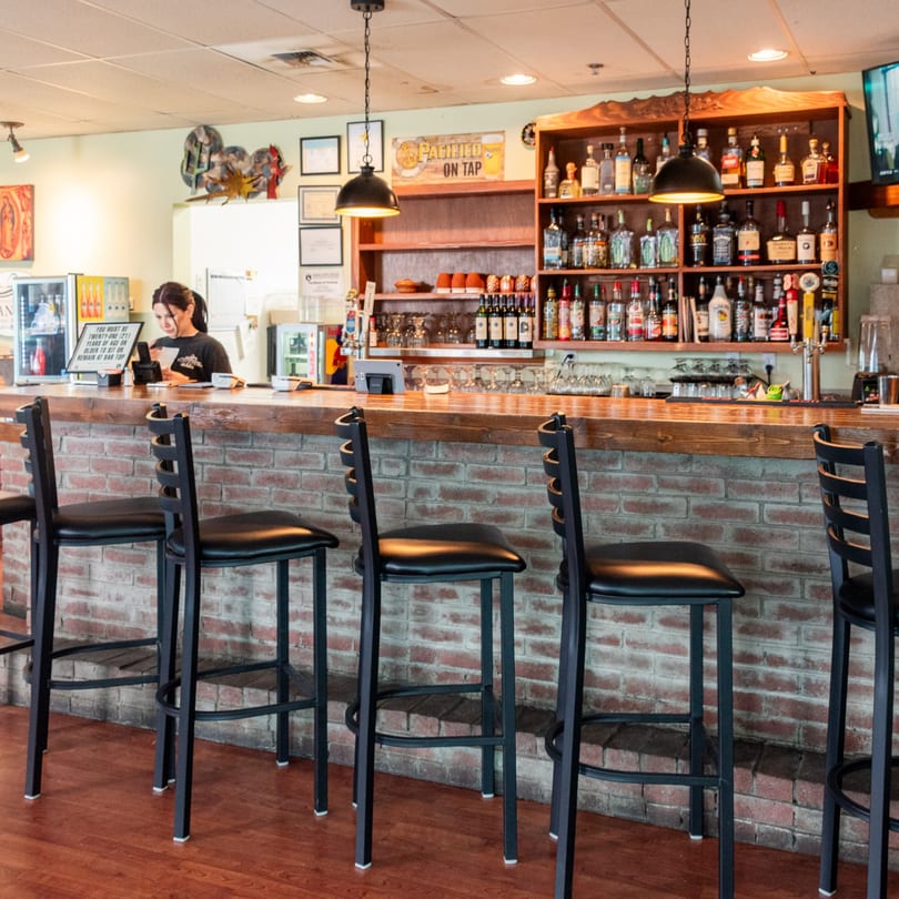 A bartender works behind a brick bar with a wooden top, lined with black bar stools.